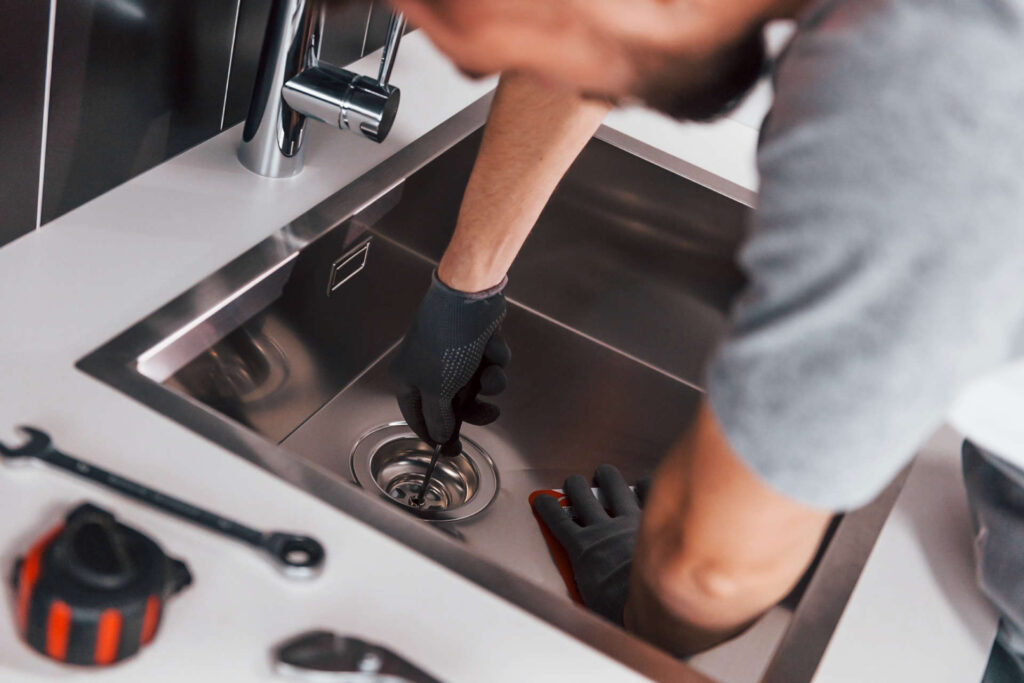 Técnico de fontanería con guantes instalando o reparando el desagüe de un fregadero de acero inoxidable.