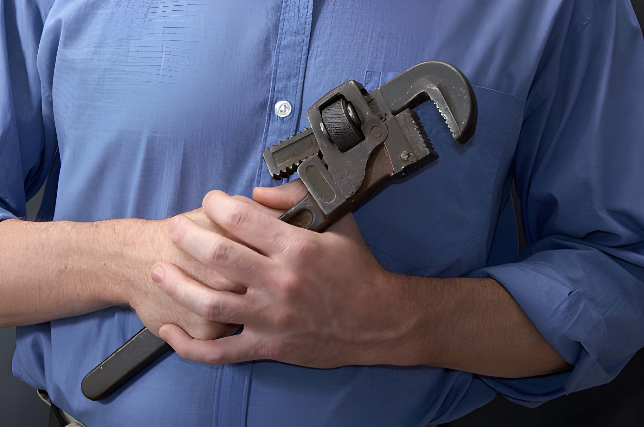 Primer plano de un hombre con camisa azul sosteniendo una llave grifa grande de metal.
